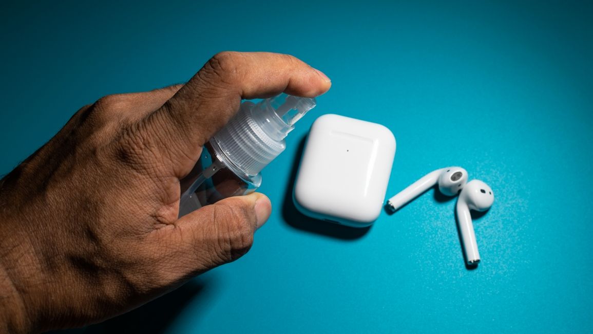 shot of a hand spraying cleaning solution over AirPods on a table shot of a hand spraying cleaning solution over AirPods on a table
