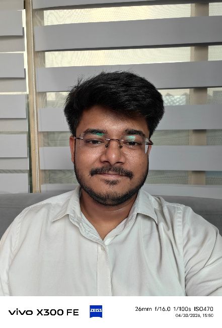 A person wearing glasses and a white shirt in front of window blinds
