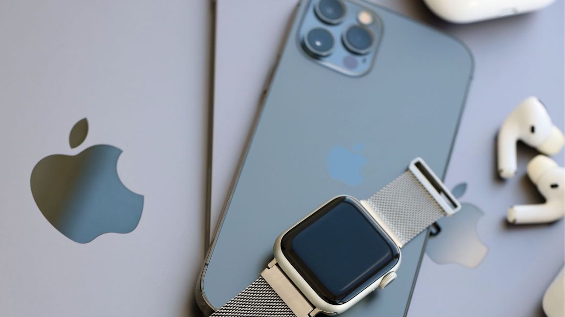 Apple watch placed on top of an iPhone with a pair of white AirPods beside them