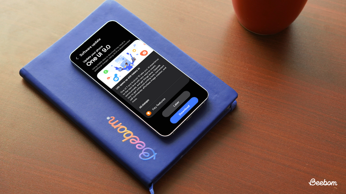 One UI 9.0 update screen on a Samsung Galaxy device lying on a blue Beebom book