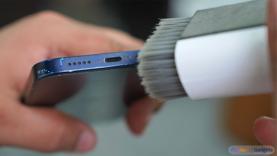 close up shot of a handheld phone showing a brush cleaning the speakers and USB port